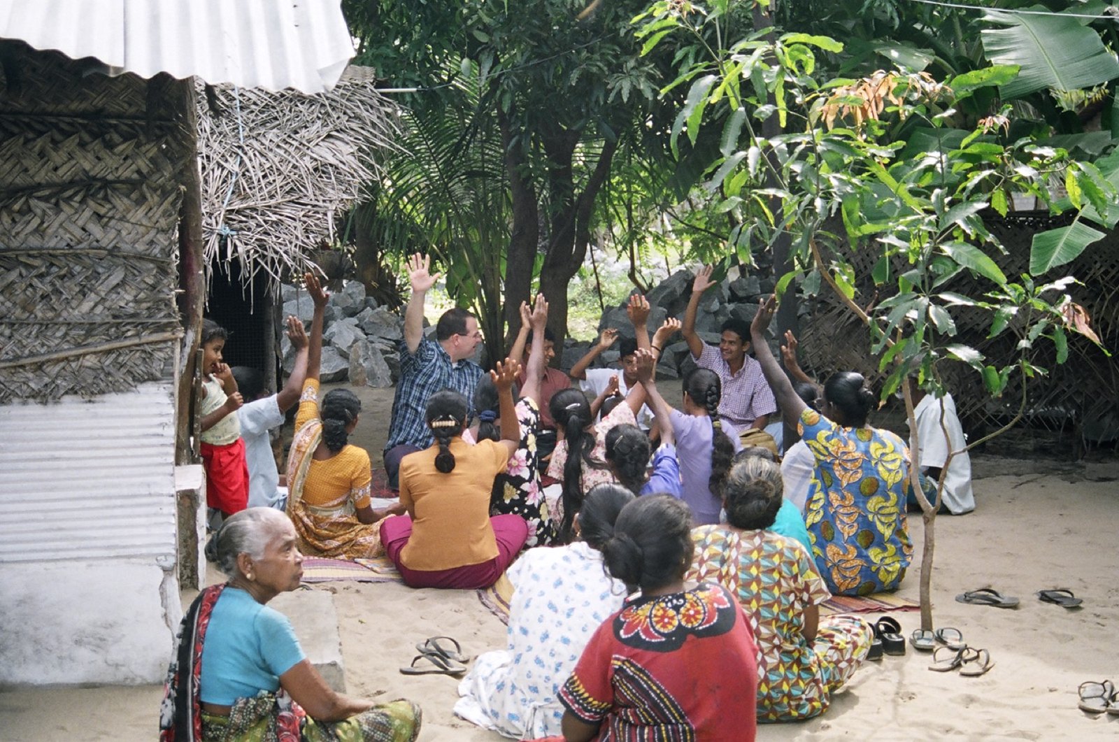 A missionary teaching a group gathered outdoors in a Sri Lankan village, many with hands raised